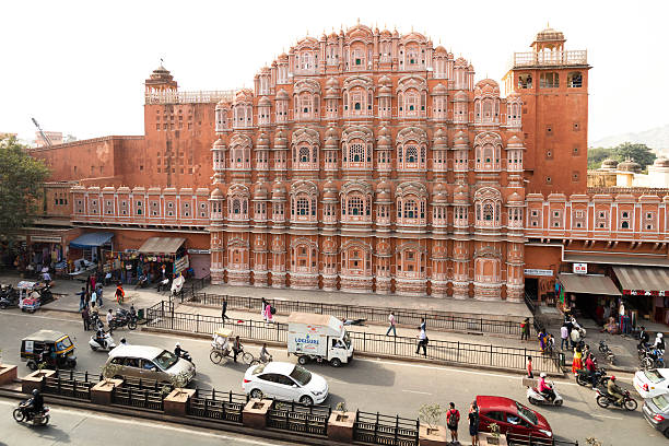 Palace of Wind, Hawa Mahal, in Jaipur, Rajasthan, India Jaipur, India - December 9, 2015: View of the Palace of Wind (Hawa Mahal). Known as the Palace of the Winds, the beautiful Hawa Mahal Facade is one of the most recognisable sights in Rajasthan, India. Busy street with cars, bikes, motorbikes, rickshaws, people and shops is visible below. maharaja express stock pictures, royalty-free photos & images