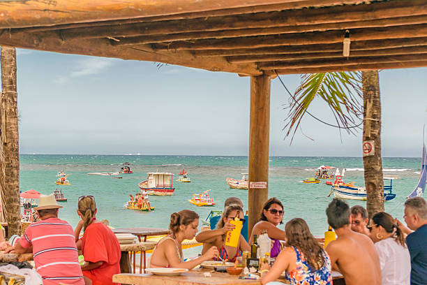 Marau, Bahia, Brasil – December, 6, 2016: unidentifiable young tanned couple holding a surfing board looking at the sea at a beach resort.