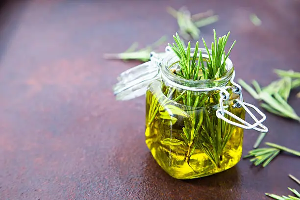 Rosemary oil. Rosemary essential oil jar glass bottle and branches of plant rosemary with flowers on rustic background.