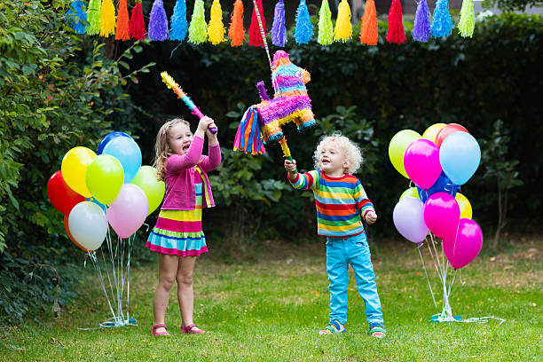 Kids playing with birthday pinata in decorated garden Kids birthday party. Group of children hitting pinata and playing with balloons. Family and friends celebrating birthday outdoors in decorated garden. Outdoor celebration with active games. toddler hitting stock pictures, royalty-free photos & images