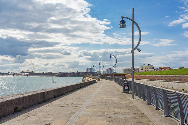 Portsmouth, England - July 14th, 2016: The Millennium walk pathway on an elevated section by the Waterfront in Old Portsmouth with sailing boats and ferries in the sea. People are walking along the pathway enjoying the nautical views. Portsmouth. Hampshire. England. 