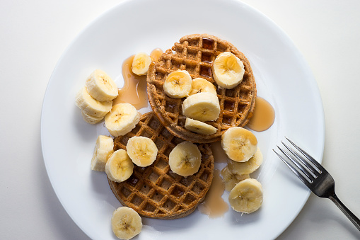 Waffle breakfast with bananas and syrup on white plate.