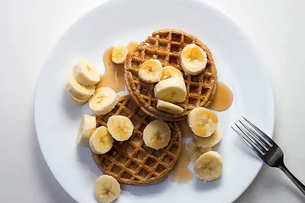 Waffle breakfast with bananas and syrup on white plate.