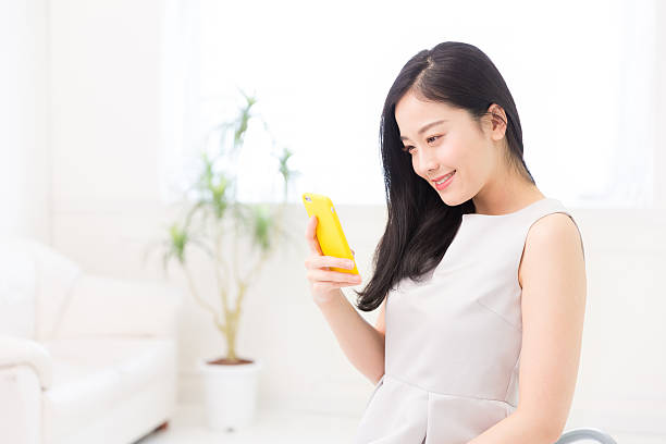 femme japonaise tenant un téléphone intelligent dans un salon - sans manches photos et images de collection