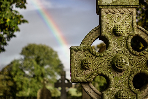 A rainbow shines behind a Celtic cross at Monasterboice, county Louth, Ireland. Intricate Celtic knot-work adorns the stone.