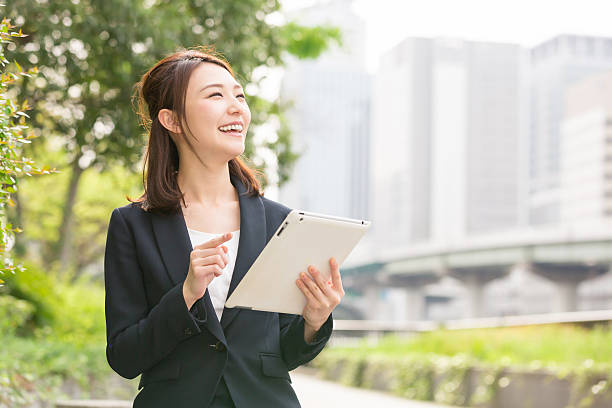 japanische geschäftsfrau hält ein tablet - women digital tablet outdoors smiling stock-fotos und bilder