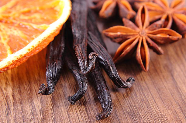 Fresh fragrant vanilla sticks pods, star anise and slices of dried orange on wooden board, seasoning for cooking or baking