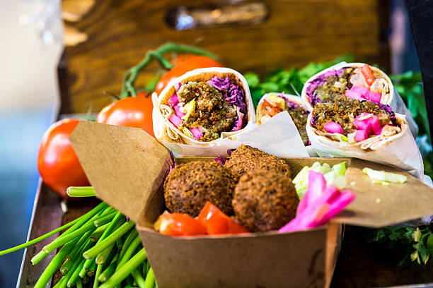 Falafel wraps and vegetarian food at Borough Market, London, UK Close up image of boxes of vegetarian food for sale on a market stall at Borough Market, a famous food market in central London, UK. In the foreground a brown cardboard box is attractively filled with falafel balls, red cabbage and tomato, whil beyond this are wraps filled with falafel, tomato and red cabbage. In the background more vegetarian food is pleasantly blurred out of focus, allowing room for copy space. Horizonal colour image. middle eastern food photos stock pictures, royalty-free photos & images