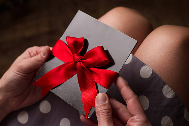 Woman hands holding a black paper card with red ribbon Close up of the hands of a woman with polka dress holding a black card with red ribbon above knees coupon photos stock pictures, royalty-free photos & images