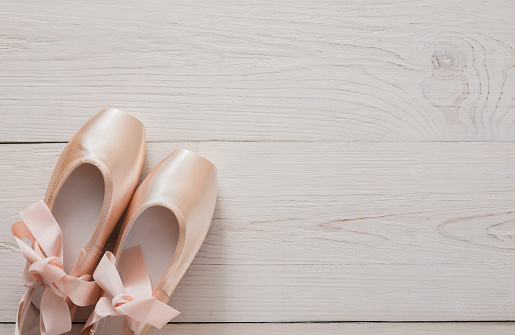 Pastel pink ballet shoes background. New pointe shoes with satin ribbon lay on white rustic shubby chic wood, top view with copy space