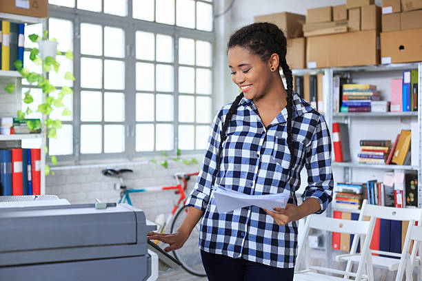 istock Smiling young african woman using copy machine in modern office 620373094