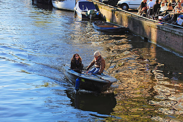 Amsterdam, Netherlands - May 1, 2016: A view along the Amsterdam Canals. Tourists riding the tourboat in a canal to see the historical buildings and natural beauty of Amsterdam. Buildings, people, bridges, cars can be seen.
