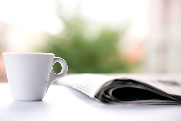 istock Close up Coffee cup and newspaper on white table outside 620379484