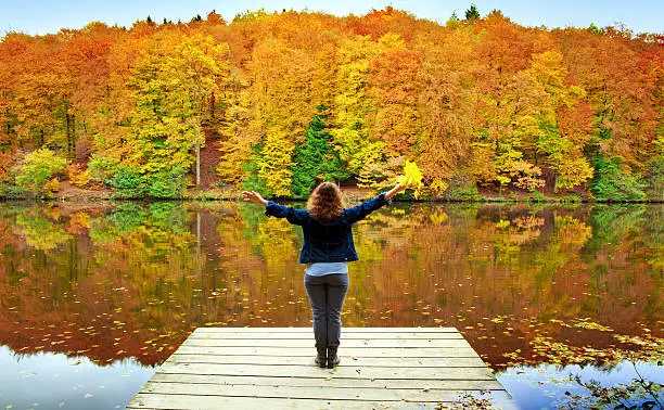 Woman stands on wooden pier by lake and beautiful landscape of nature in autumn.