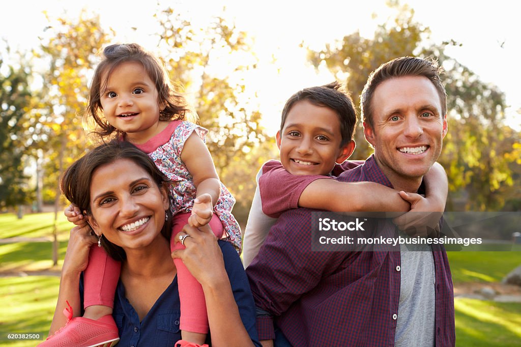 Mixed race parents carry their kids piggyback in a park Family Stock Photo