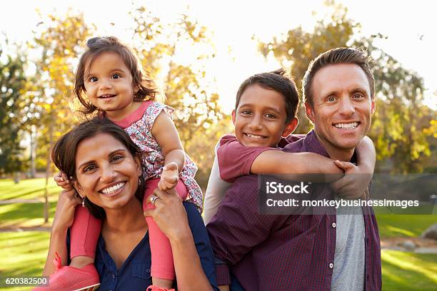 Mixed Race Parents Carry Their Kids Piggyback In A Park Stock Photo - Download Image Now