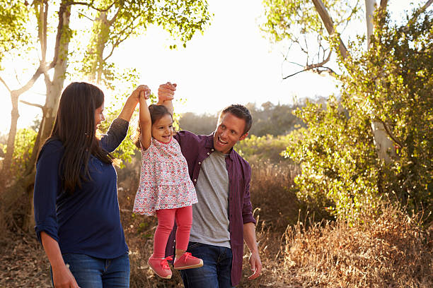 istock Mixed race couple walk on rural path lifting young daughter 620382562