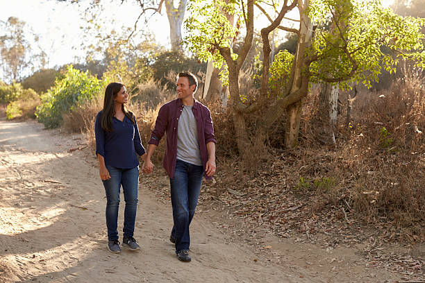 istock Mixed race couple walking in park holding hands, front view 620382564