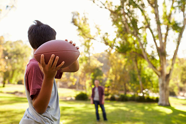 istock Young boy throwing ball to dad in park, focus on foreground 620382690
