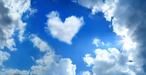 heart shaped cloud over cloudy and sunny sky with sunbeam