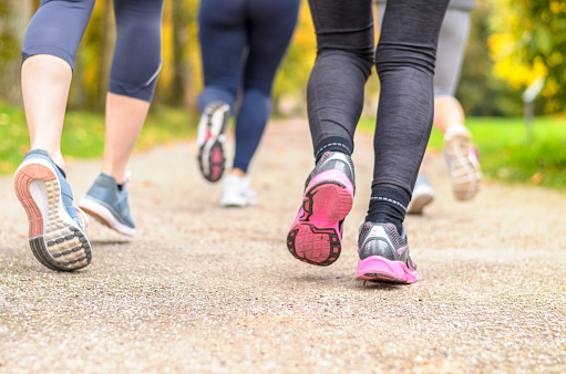 Group of young woman jogging together in a park with a close up low angle view from behind of their lower legs and running shoes