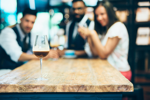 Wine glass with fresh brewed coffee on wooden table.Defocused people on background.