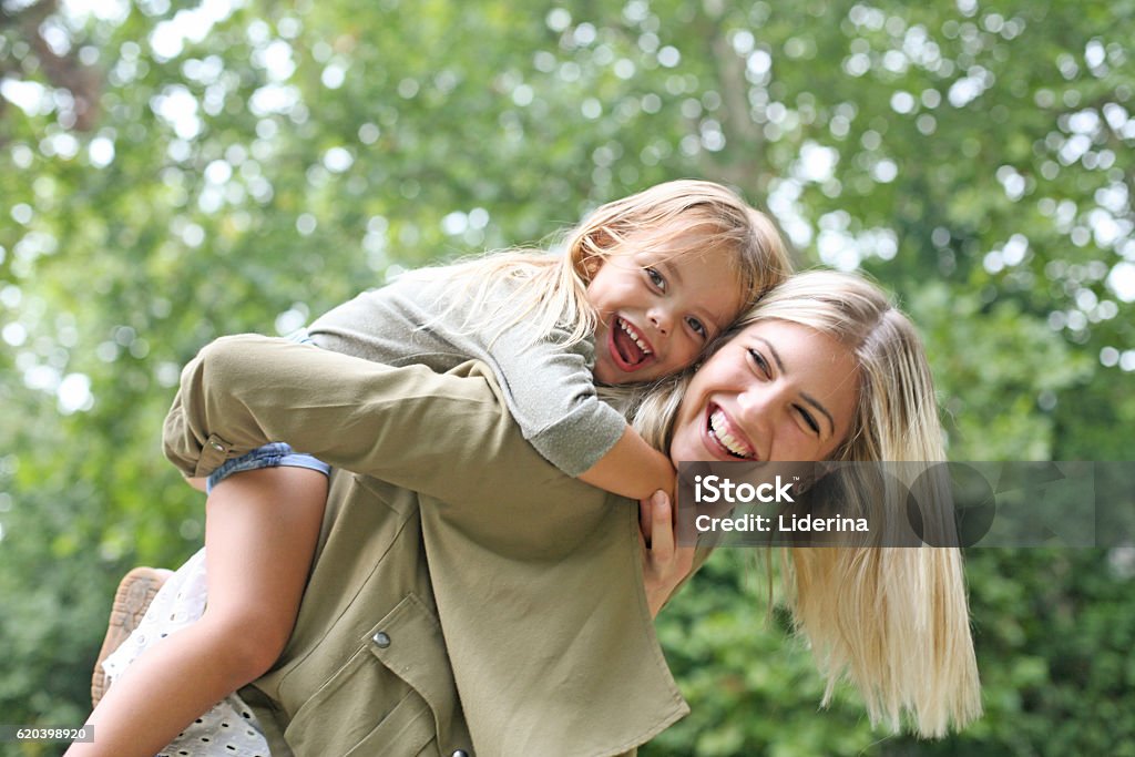 Little girl on a piggy back ride with her mother. Cute young daughter on a piggy back ride with her mother Family Stock Photo