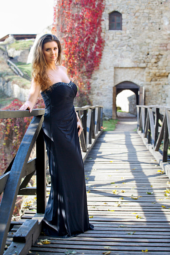 Young beautiful woman is standing on wood bridge in front of ruins. Autumnal atmosphere.