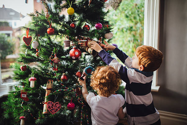 Helping mum with the tree A young red head boy and his sister are decorating the Christmas tree in their home. He is reaching up and putting a bauble onto the tree while his sister tries to help. decorating stock pictures, royalty-free photos & images