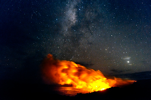 This is a horizontal, royalty free stock photograph of the lava flowing from Kilauea volcano at night in Volcanoes National Park on the Big Island of Hawaii. The Milky Way is visible in the starry, night sky background. Photographed with a Nikon D800 DSLR camera.
