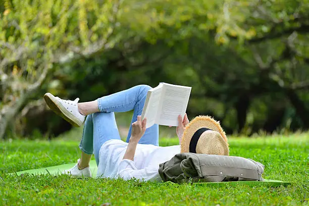 Photo of Woman lying on green grass reading a book