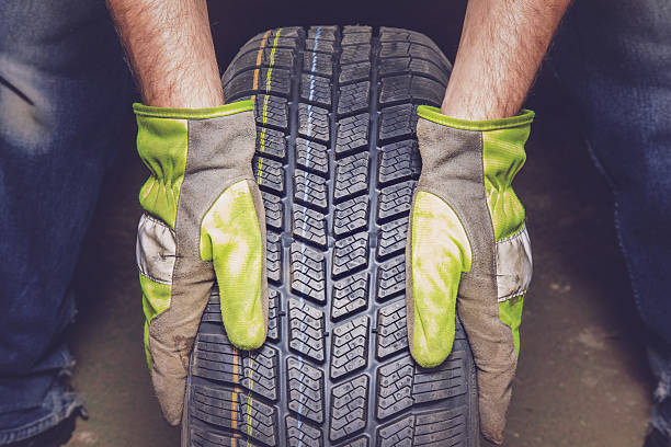 Man holding new, black rubber tire in the garage. Man's hands in gloves holding new rubber tire in the garage. Seasonal tire change. tire vehicle part stock pictures, royalty-free photos & images