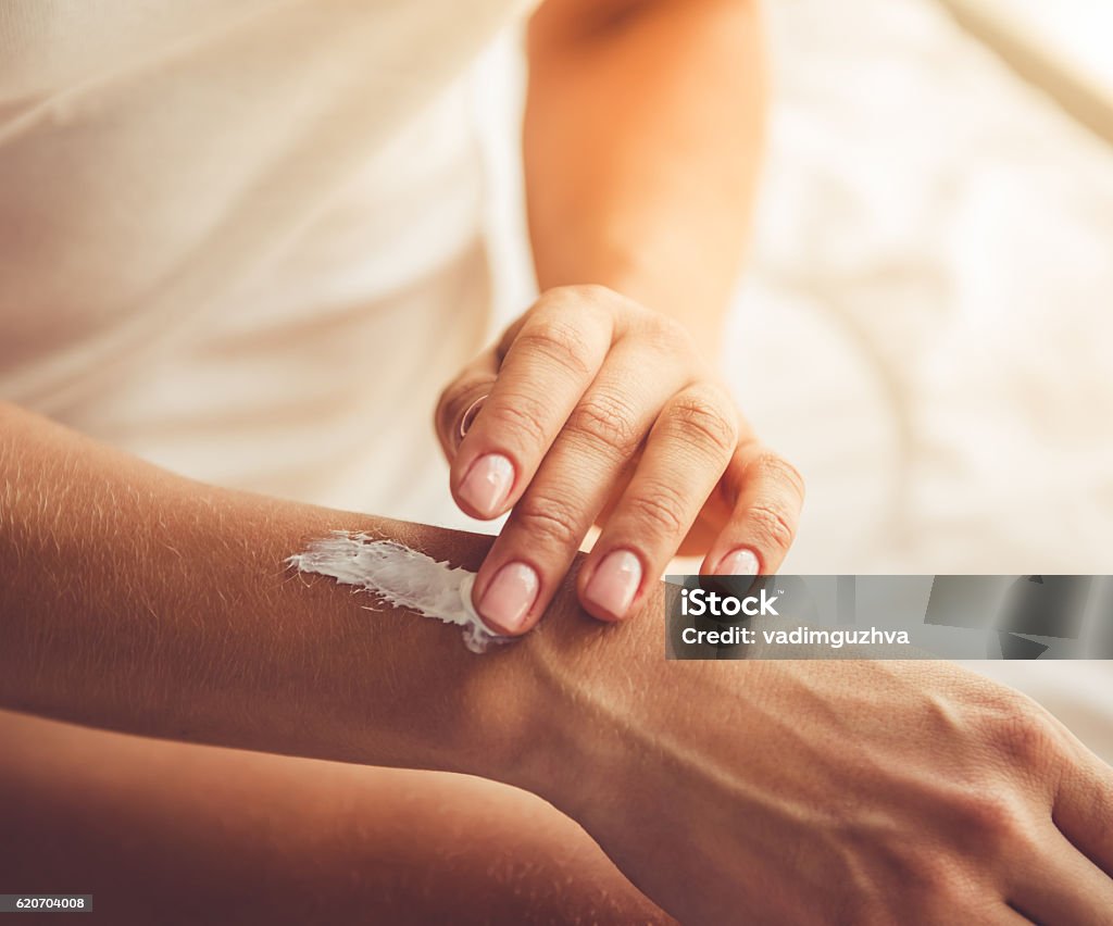 Beautiful young lady at home Cropped image of beautiful young woman applying hand cream while sitting on bed at home Moisturizer Stock Photo