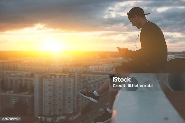 Man Sitting On The Edge Of The Roof With Smartphone Stock Photo - Download Image Now