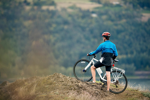 Adult male trail bike rider looking over valley wearing bike helmet and biking attire