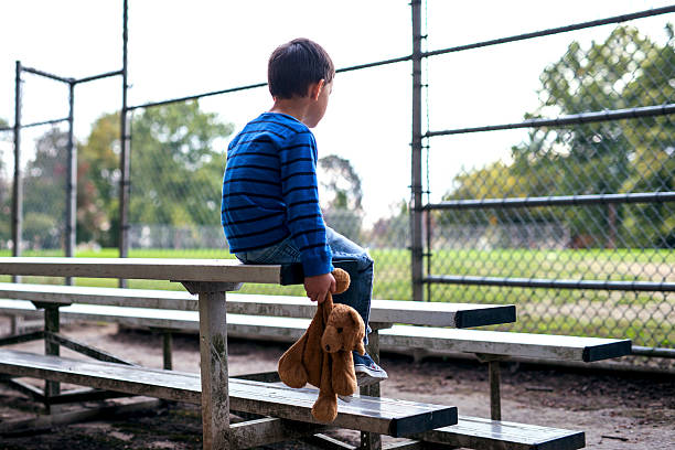 istock Young boy sitting alone on bleachers holding a teddy bear 620713802