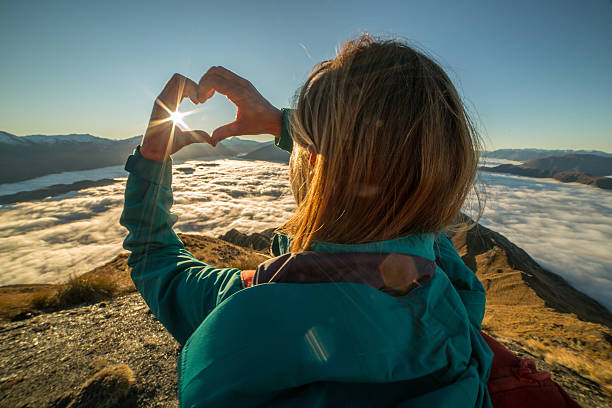 istock Woman on mountain summit makes heart shape finger frame 620717832