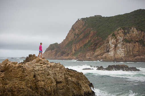 Sporty woman stands on the rocks and watches the view over the sea
