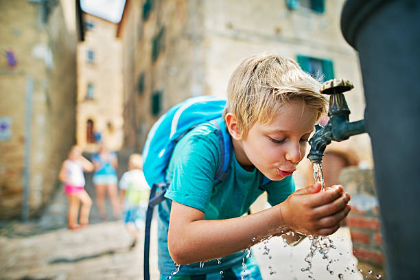 Little tourist drinking water from public fountain Family is visiting beautiful italian town. The boy is splashing his face and drinking from the public fountain. Mother and other kids are visible in the background. young hot stock pictures, royalty-free photos & images