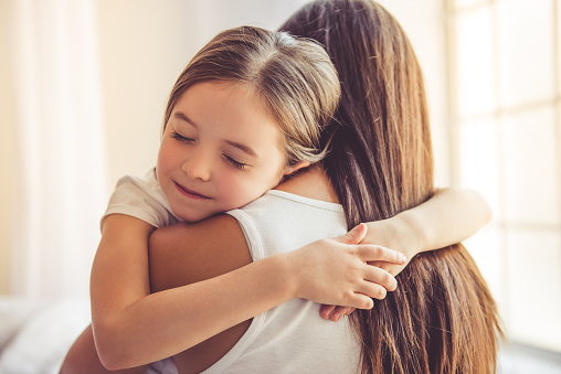 Beautiful young woman and her charming little daughter are hugging and smiling