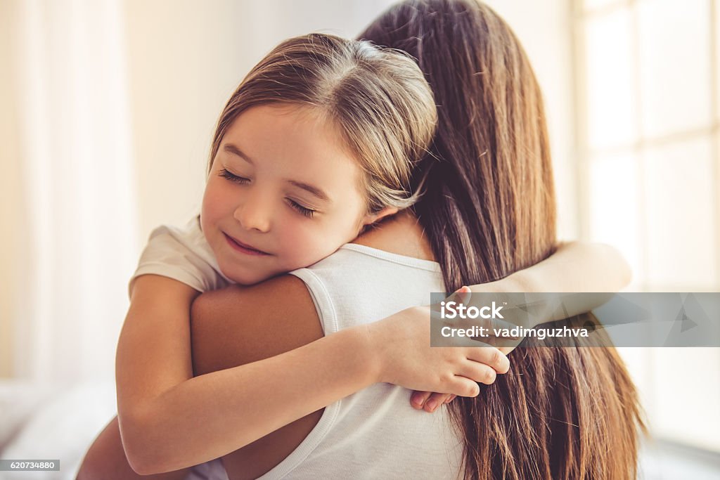 Mother and daughter at home Beautiful young woman and her charming little daughter are hugging and smiling Embracing Stock Photo