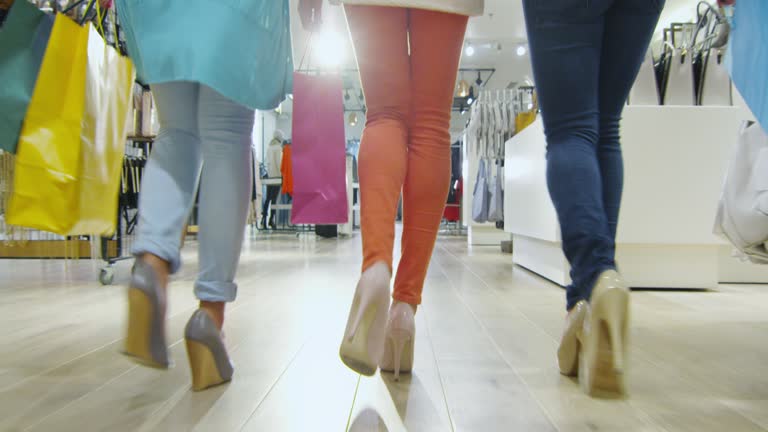 Low shot of three girls that are walking through a clothing store in colorful garments.