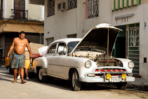 Havana, Сuba - April 17, 2016: A man working on vintage American car, (1952 Chevrolet Styleline Deluxe), on the street, next to residential buildings, Old Havana, Cuba