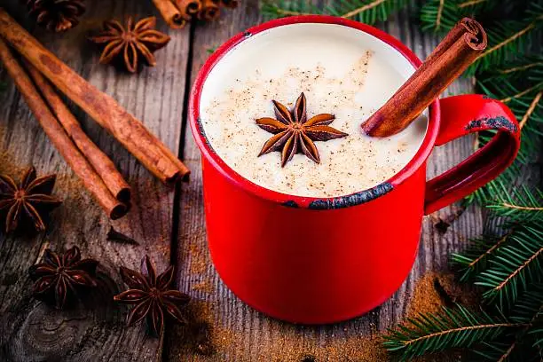 Christmas drink: hot white chocolate with cinnamon and star anise in red mug on wooden rustic background