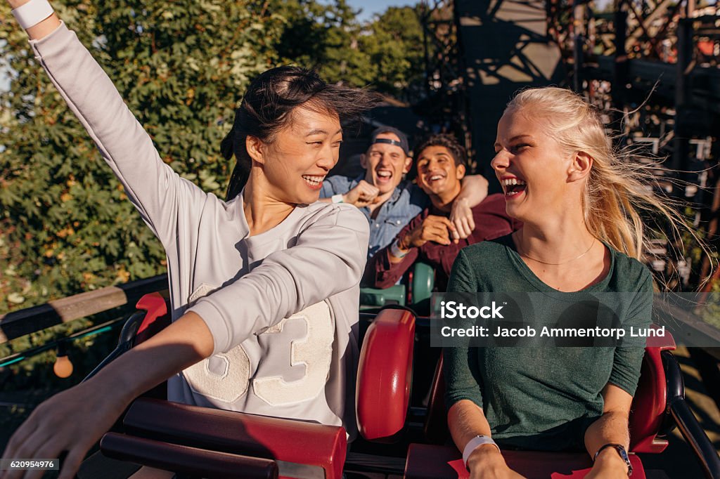 Friends enjoying and cheering on roller coaster Shot of young friends enjoying and cheering on roller coaster ride. Young people having fun on rollercoaster at amusement park. Rollercoaster Stock Photo