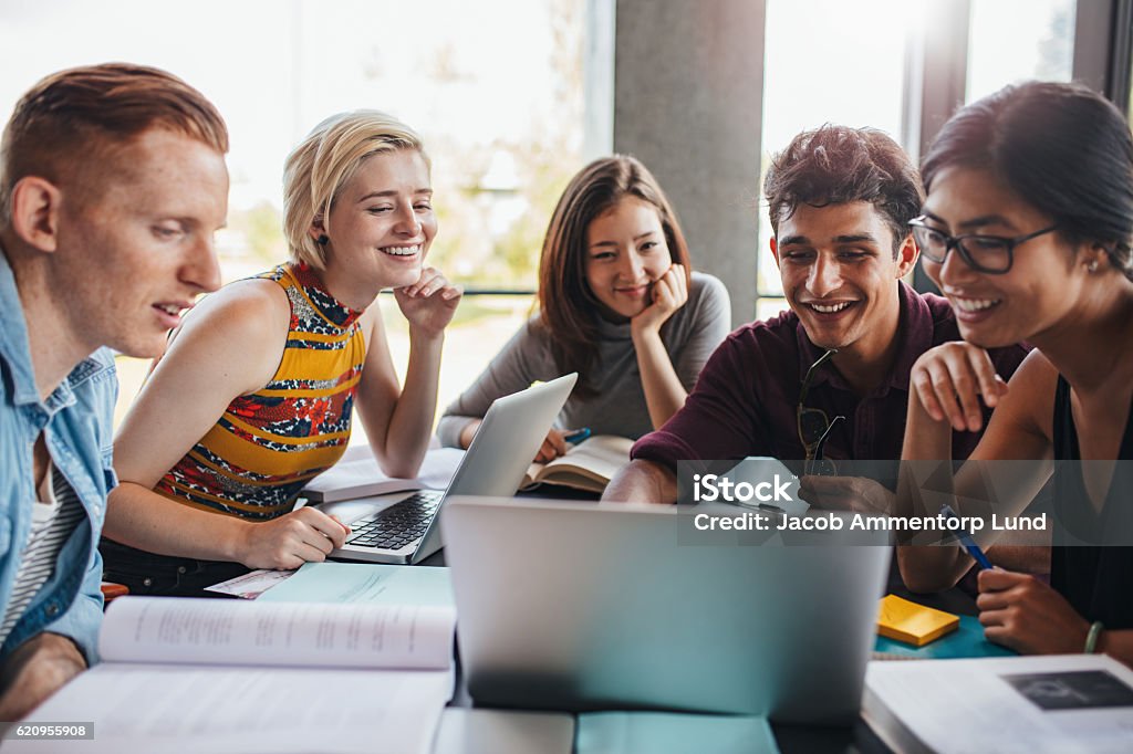 Group of students studying in the library Multiracial group of young students studying in the library. Young people sitting together at table with books and laptop for researching information for their project. University Student Stock Photo