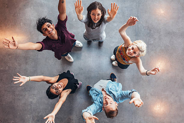 Young students celebrating success Top view of young students standing together looking up at camera with their hands raised in celebration. cheering group of people success looking at camera stock pictures, royalty-free photos & images