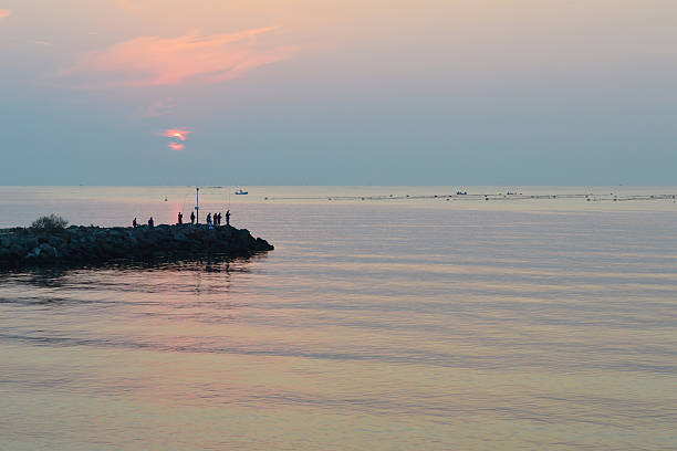 Ravda, Bulgaria - September 15, 2016: Peaceful summer morning, calm sea at sunrise, silhouettes of fishermen on breakwater, fish farm in the distance