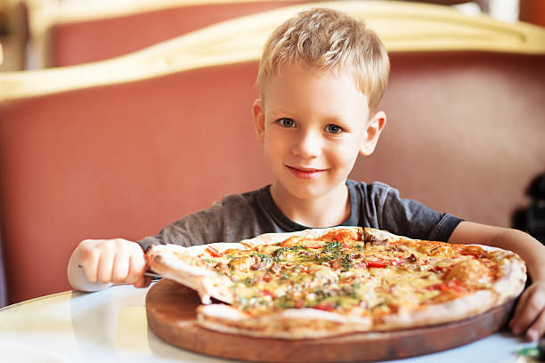 adorabile ragazzino che mangia pizza in un ristorante - pizzeria cafe restaurant italian culture foto e immagini stock