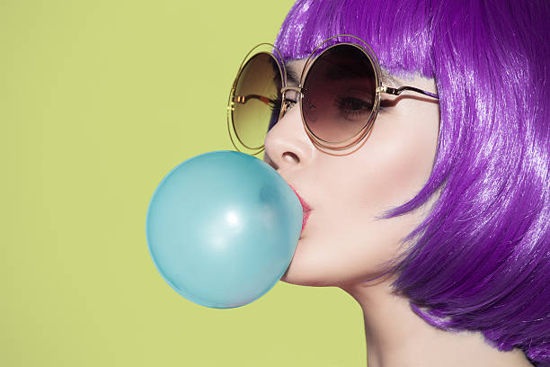 Pop art woman portrait blowing a blue bubble chewing gum Pop art woman portrait wearing purple wig. Blow a blue bubble chewing gum. Olive background. bubble gum photos stock pictures, royalty-free photos & images